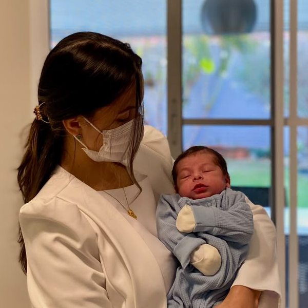 Dra. Amanda Rocha com um recém-nascido no colo, em atendimento domiciliar