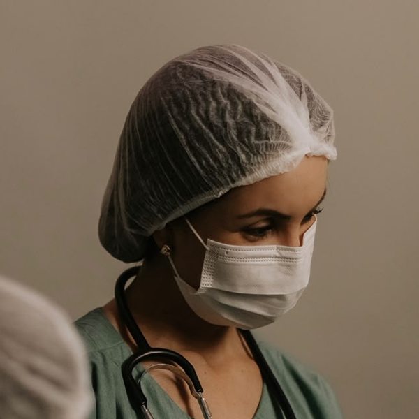 Dra. Amanda Rocha de touca, máscara e estetoscópio, atenta durante um atendimento